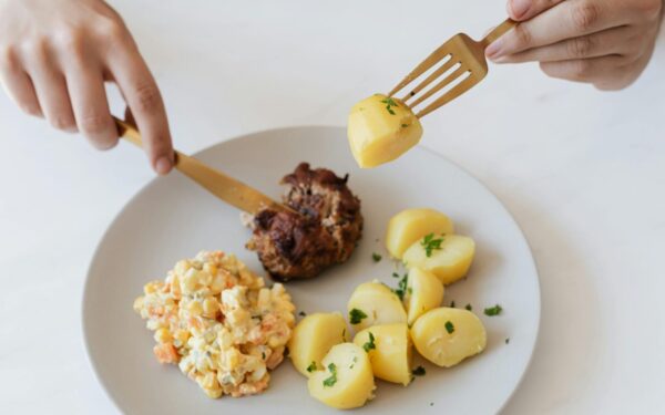 From above of crop anonymous person with cutleries eating delicious fried cutlet and hot boiled potatoes with parsley garnished with nutritious Russian salad