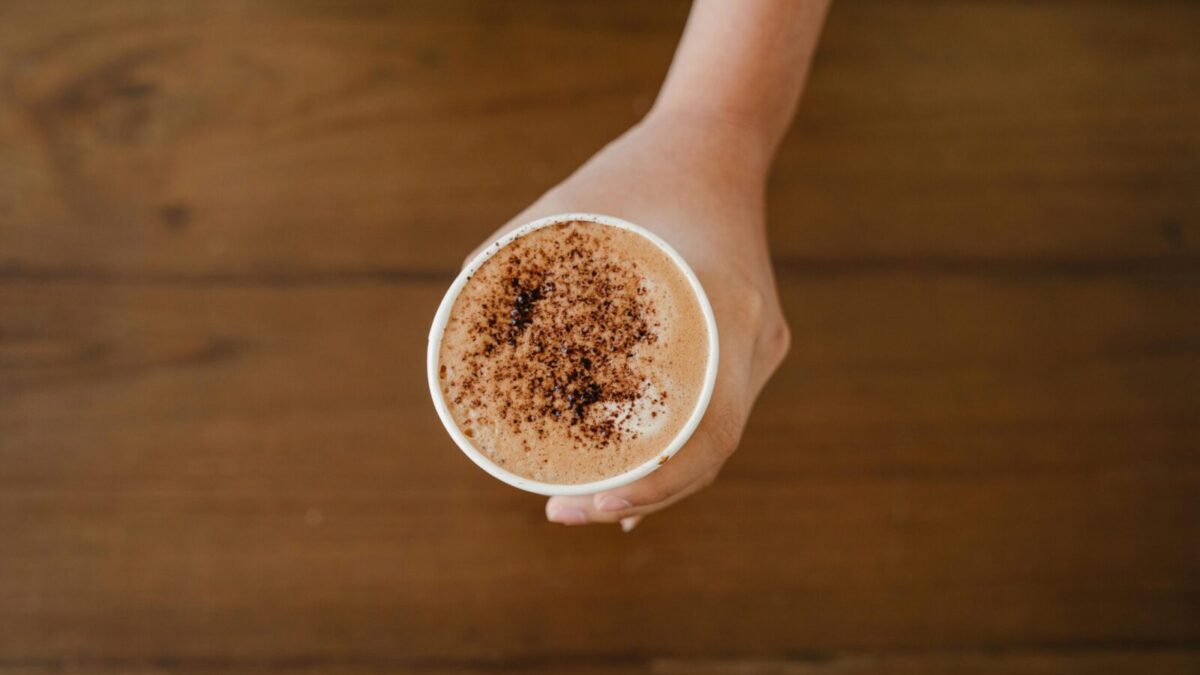 A hand holding a cappuccino cup topped with cocoa powder, captured from above.