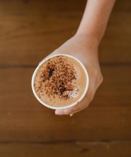 A hand holding a cappuccino cup topped with cocoa powder, captured from above.