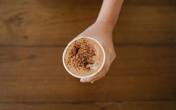 A hand holding a cappuccino cup topped with cocoa powder, captured from above.