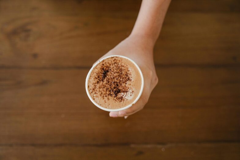 A hand holding a cappuccino cup topped with cocoa powder, captured from above.
