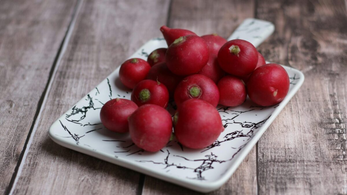From above of fresh whole crunchy radishes on ornamental plate on wooden table at home