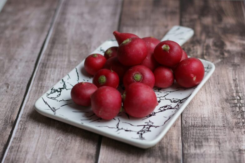 From above of fresh whole crunchy radishes on ornamental plate on wooden table at home
