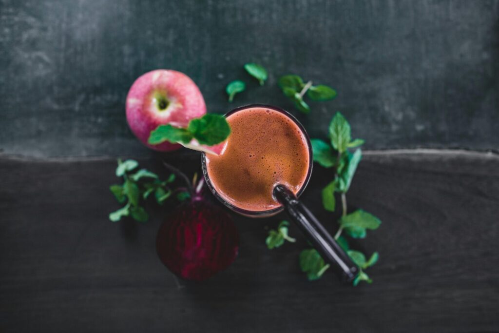Top view glass of cold pressed juice composed with fresh apple and beetroot and decorated with mint leaves
