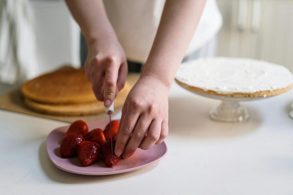 Hands slicing strawberries for a delicious homemade cake.