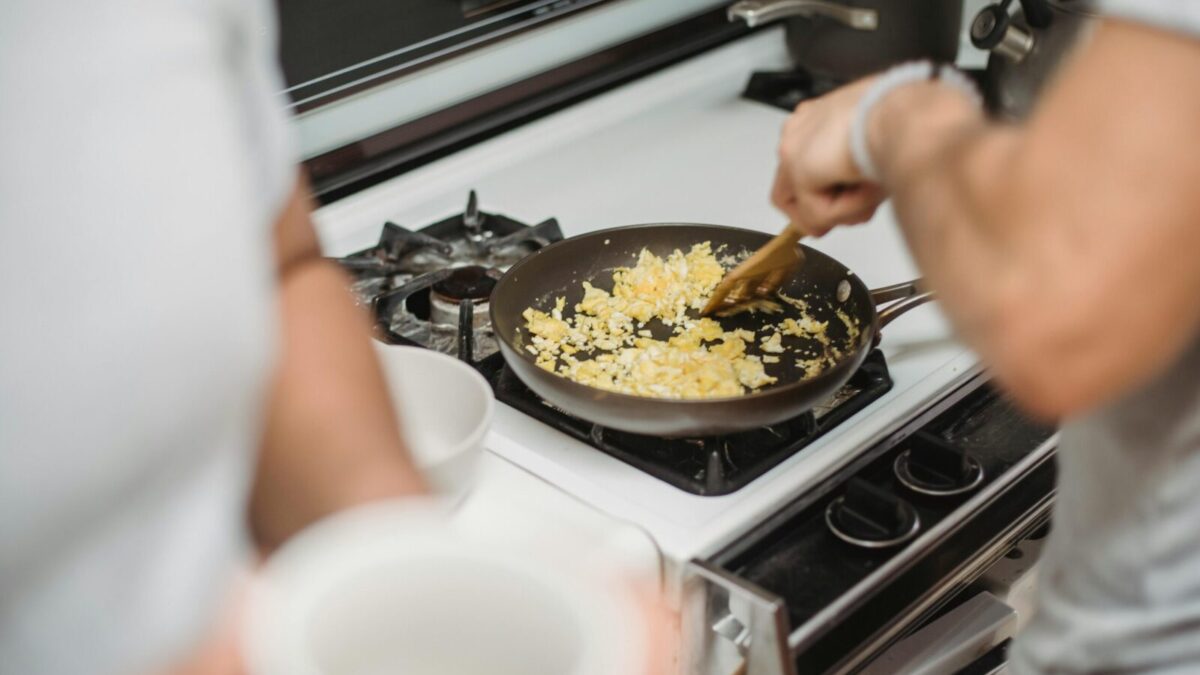 Close-up of a person cooking scrambled eggs on a stovetop, highlighting a cozy kitchen setting.