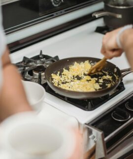 Close-up of a person cooking scrambled eggs on a stovetop, highlighting a cozy kitchen setting.