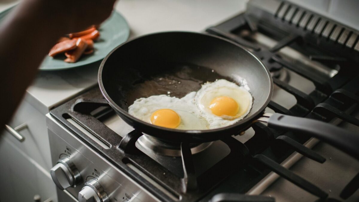 Close-up of two fried eggs cooking in a frying pan on a modern stovetop.