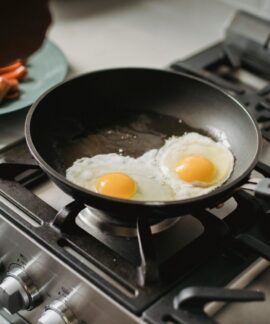 Close-up of two fried eggs cooking in a frying pan on a modern stovetop.