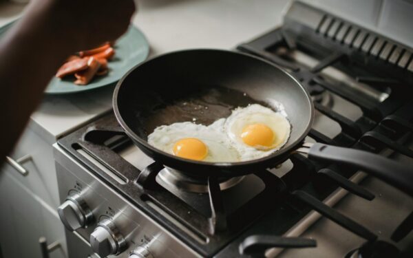 Close-up of two fried eggs cooking in a frying pan on a modern stovetop.
