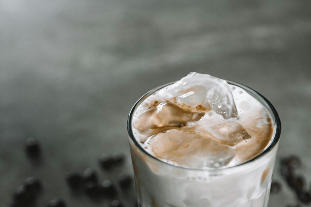 Close-up of a chilled iced coffee with frothy milk and ice cubes in a glass against a muted background.