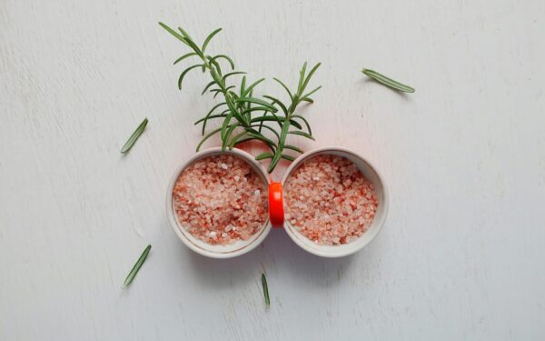 Top view of pink Himalayan salt and fresh rosemary in bowls on white table.