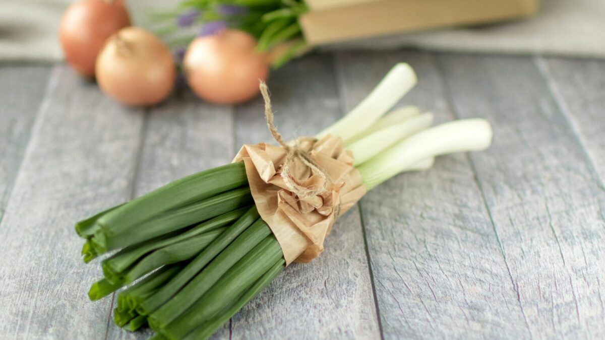 A bundle of fresh leeks and onions on a rustic wooden surface, ideal for cooking inspiration.