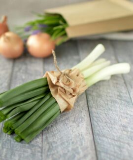 A bundle of fresh leeks and onions on a rustic wooden surface, ideal for cooking inspiration.