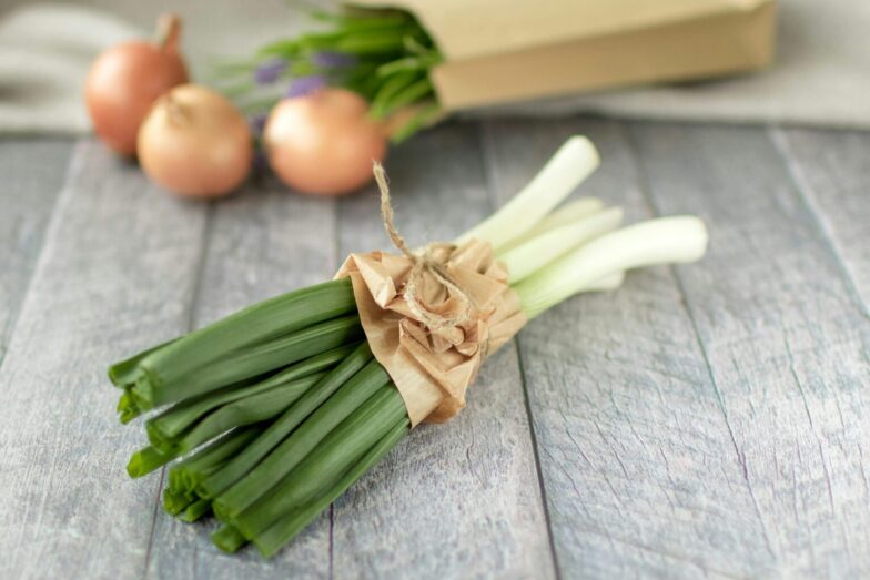 A bundle of fresh leeks and onions on a rustic wooden surface, ideal for cooking inspiration.