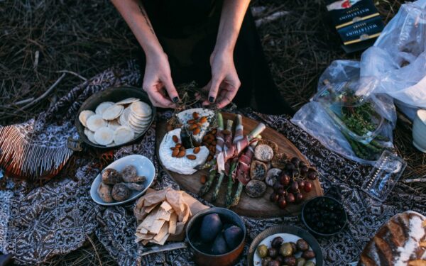 From above crop anonymous female serving yummy food including asparagus with bacon potatoes and grapes on wooden board placed on plaid during picnic in nature