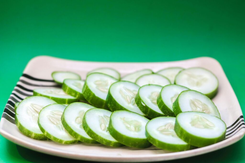 Close-up of sliced cucumbers arranged on a striped plate with a green background.