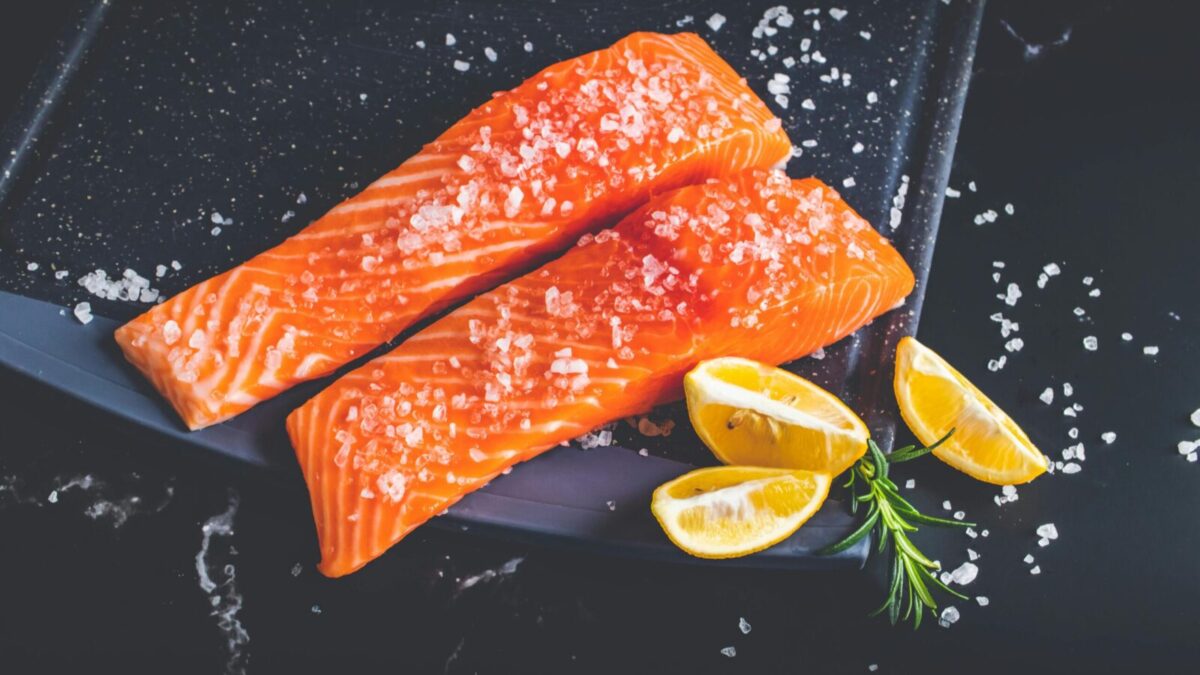 Close-up of raw salmon fillets garnished with salt, lemon wedges, and rosemary on a baking tray.