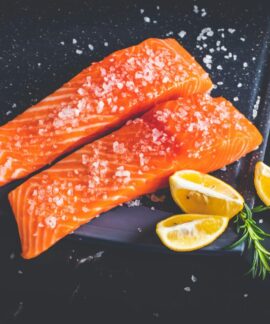 Close-up of raw salmon fillets garnished with salt, lemon wedges, and rosemary on a baking tray.