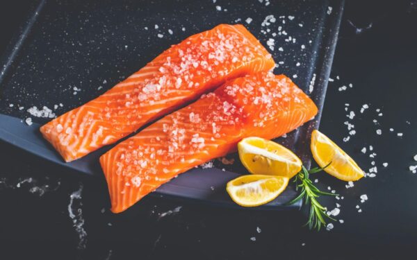 Close-up of raw salmon fillets garnished with salt, lemon wedges, and rosemary on a baking tray.