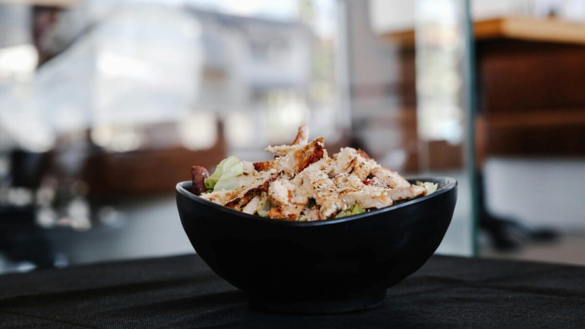 Savor this close-up of a grilled chicken salad in a stylish black bowl indoors.