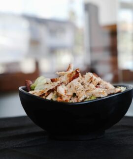 Savor this close-up of a grilled chicken salad in a stylish black bowl indoors.