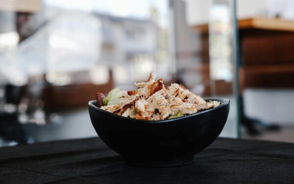 Savor this close-up of a grilled chicken salad in a stylish black bowl indoors.