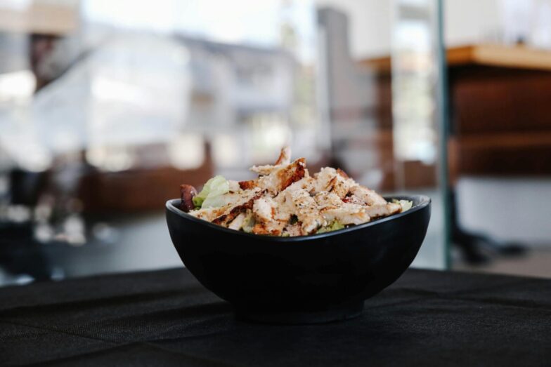 Savor this close-up of a grilled chicken salad in a stylish black bowl indoors.