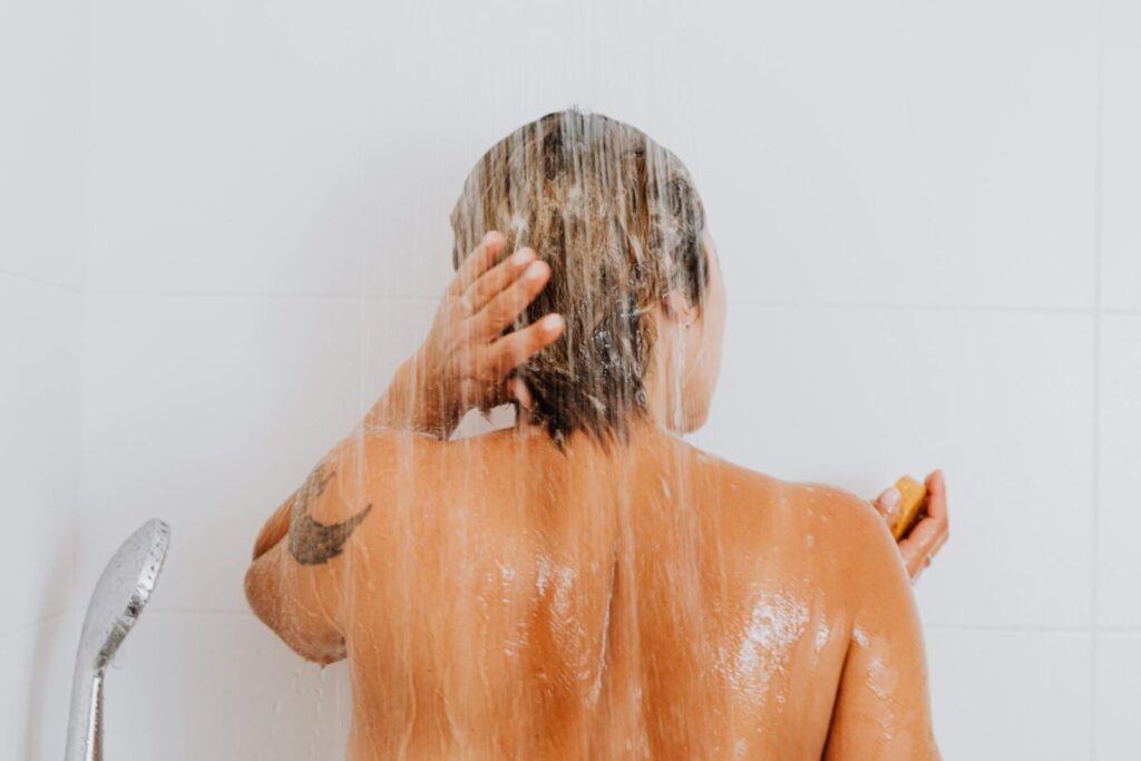 Rear view of a woman rinsing hair under shower, capturing an intimate and refreshing moment indoors.