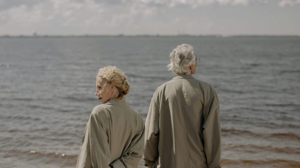 A senior couple in trench coats enjoying a tranquil day by the sea, gazing at the ocean horizon.