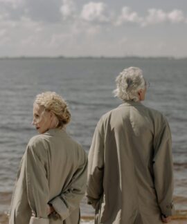 A senior couple in trench coats enjoying a tranquil day by the sea, gazing at the ocean horizon.