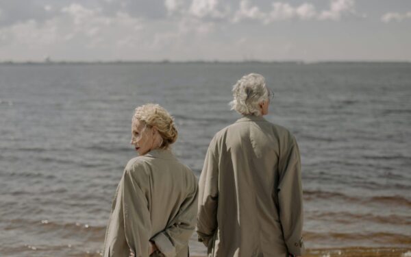 A senior couple in trench coats enjoying a tranquil day by the sea, gazing at the ocean horizon.