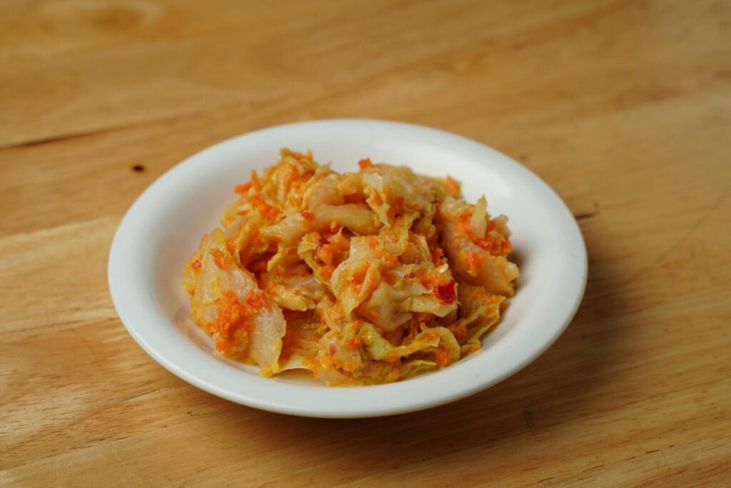 Savory Korean kimchi served in a classic white ceramic bowl on a wooden table.