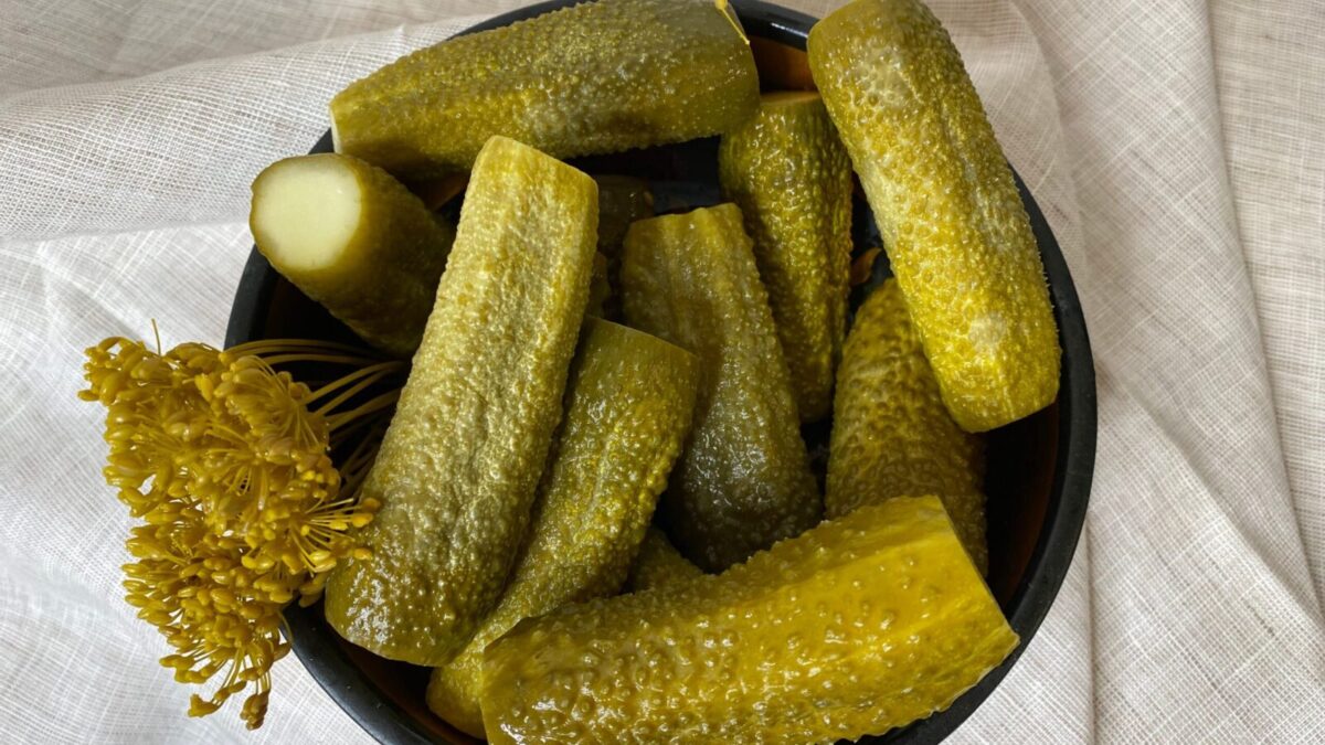 A bowl filled with freshly made dill pickles, showcasing vibrant green hues accompanied by dill flowers on a cloth backdrop.