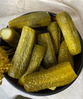 A bowl filled with freshly made dill pickles, showcasing vibrant green hues accompanied by dill flowers on a cloth backdrop.