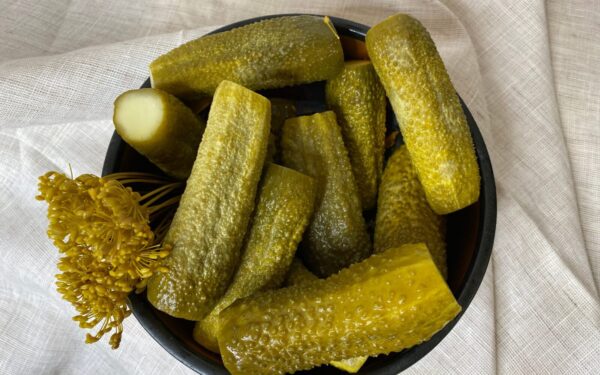 A bowl filled with freshly made dill pickles, showcasing vibrant green hues accompanied by dill flowers on a cloth backdrop.