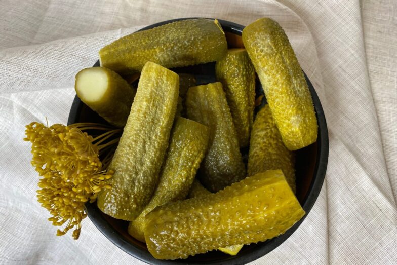 A bowl filled with freshly made dill pickles, showcasing vibrant green hues accompanied by dill flowers on a cloth backdrop.
