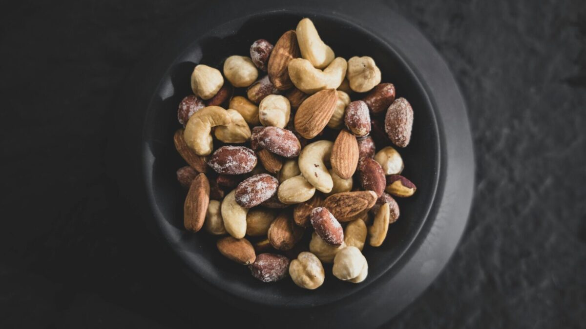 Top view of a variety of mixed nuts in a black bowl, showcasing almonds, cashews, and hazelnuts.