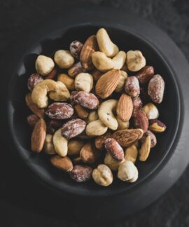 Top view of a variety of mixed nuts in a black bowl, showcasing almonds, cashews, and hazelnuts.