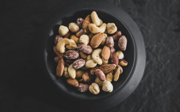 Top view of a variety of mixed nuts in a black bowl, showcasing almonds, cashews, and hazelnuts.