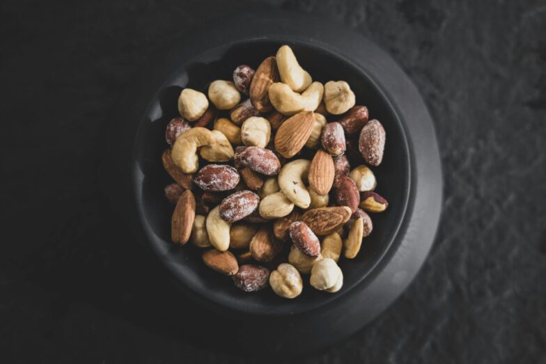 Top view of a variety of mixed nuts in a black bowl, showcasing almonds, cashews, and hazelnuts.