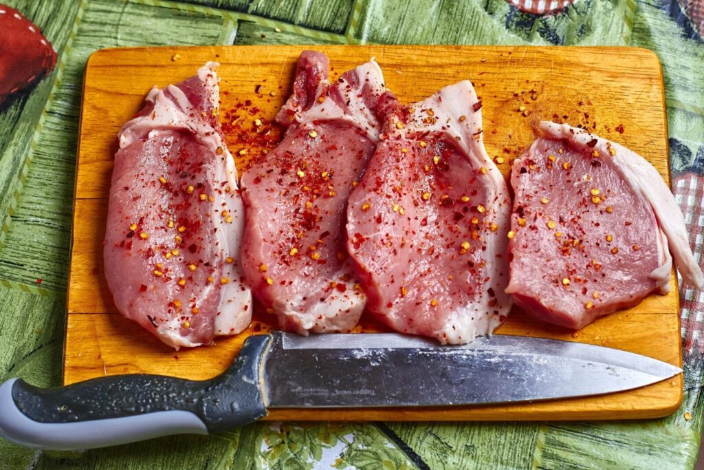 Freshly seasoned pork chops with spices on a wooden chopping board, ready for cooking.