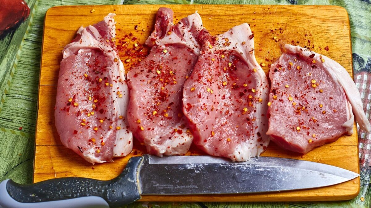 Freshly seasoned pork chops with spices on a wooden chopping board, ready for cooking.