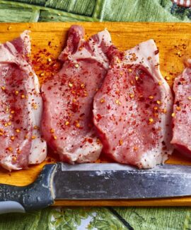 Freshly seasoned pork chops with spices on a wooden chopping board, ready for cooking.