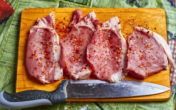 Freshly seasoned pork chops with spices on a wooden chopping board, ready for cooking.