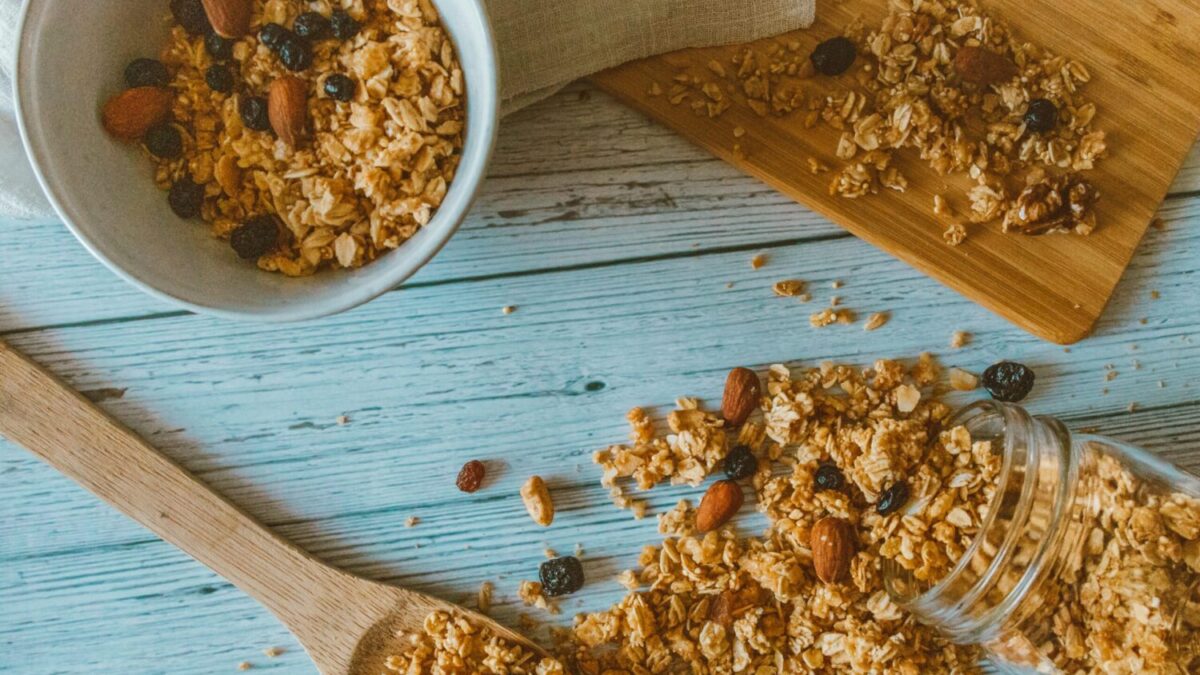 Top view of granola with almonds and berries spilled from a jar onto a wooden table.
