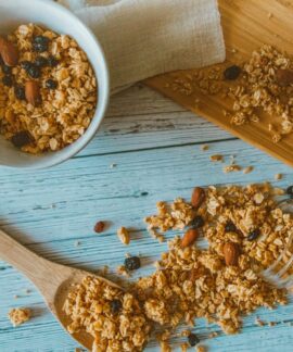 Top view of granola with almonds and berries spilled from a jar onto a wooden table.