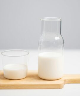 A minimalist image of milk in a glass and pitcher on a wooden board for a fresh, modern look.