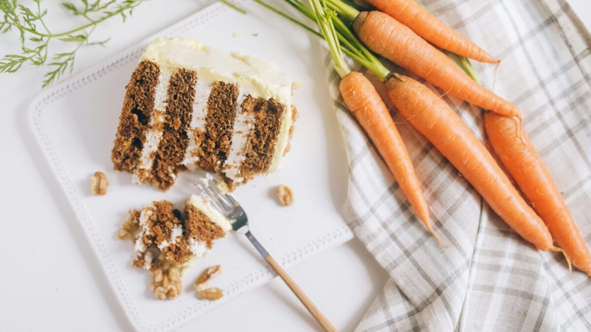 A slice of carrot cake with cream cheese frosting and fresh carrots beautifully arranged.
