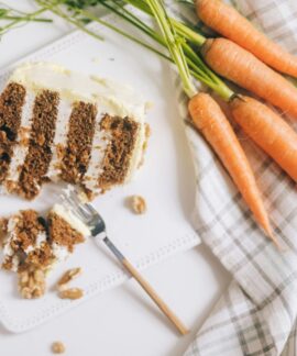 A slice of carrot cake with cream cheese frosting and fresh carrots beautifully arranged.